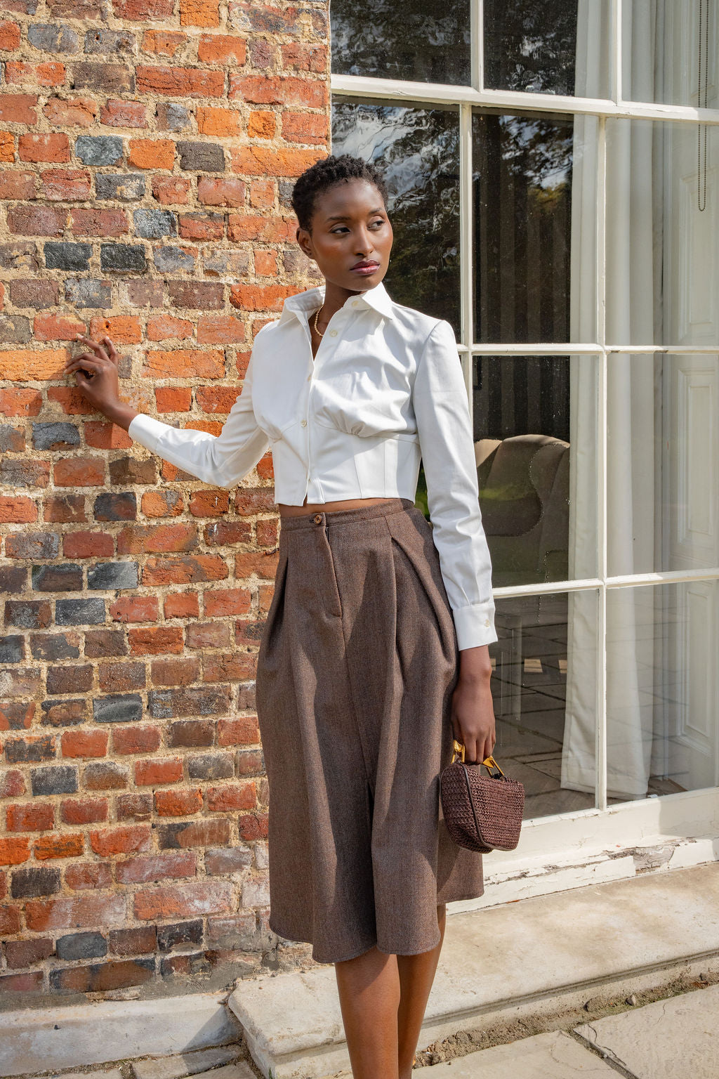 Brown wool midi skirt with pleats, paired with white button-up shirt and brown handbag.