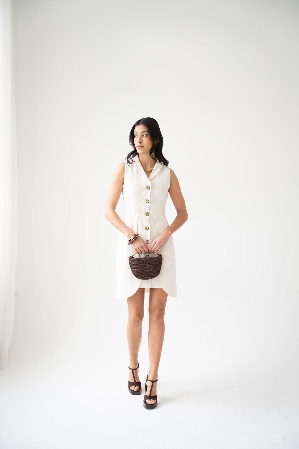 Cream sleeveless shirt dress with front buttons and collar, worn with black platform sandals and a small brown handbag.