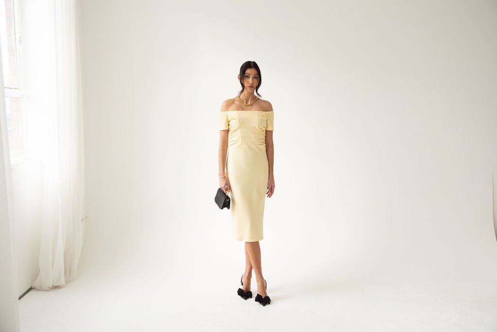 Light yellow off-the-shoulder midi dress with ruched bodice and fitted skirt.