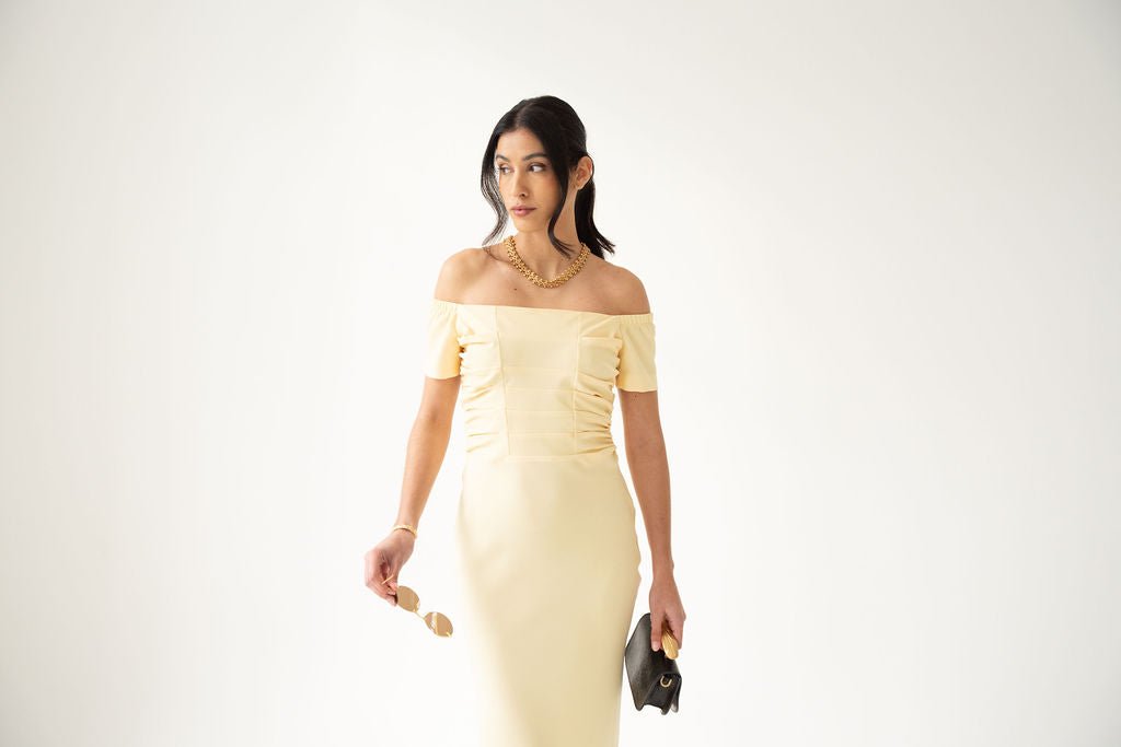 Pale yellow off-the-shoulder midi dress with ruched front and fitted silhouette.