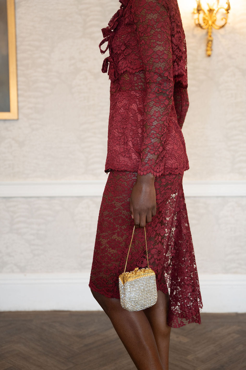 Burgundy lace midi dress with long sleeves and scalloped hem paired with a small beaded handbag.