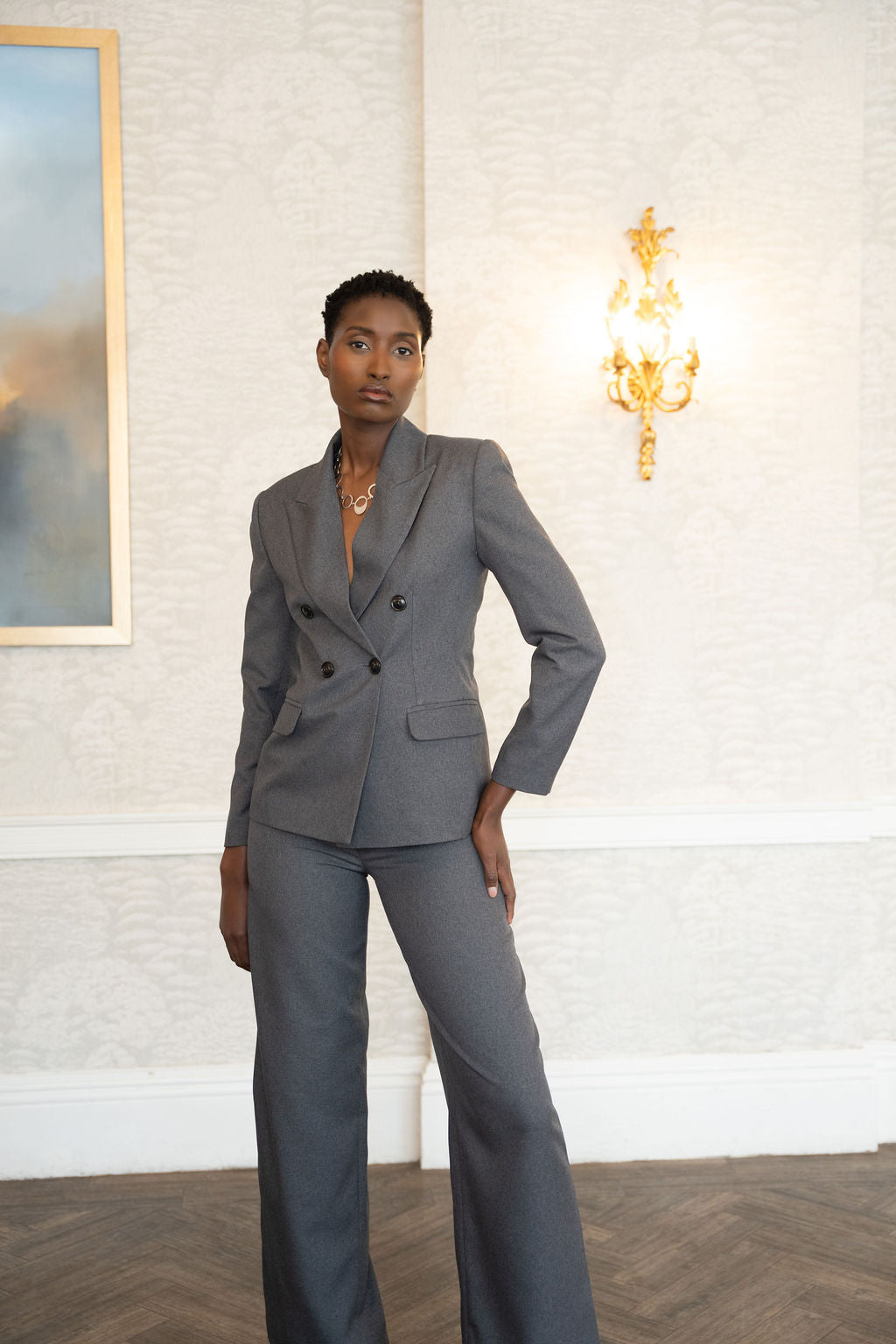 Grey double-breasted blazer with peak lapels and structured shoulders, paired with matching wide-leg trousers.
