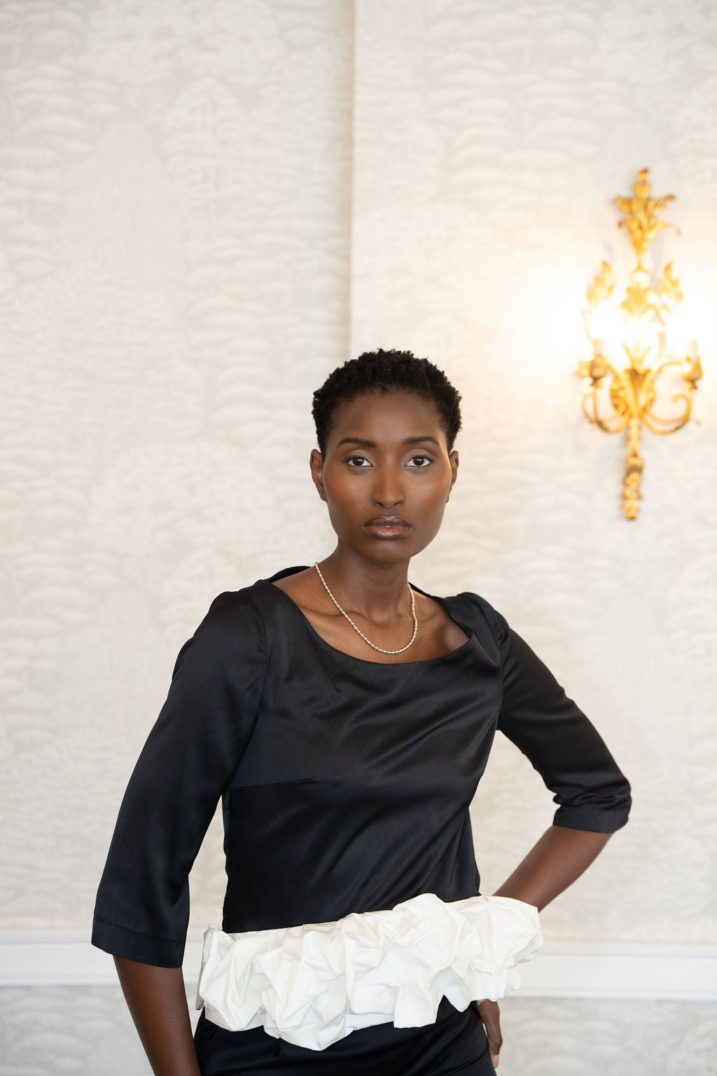 Black satin top with three-quarter sleeves and a gathered white ruffle detail at the waist.