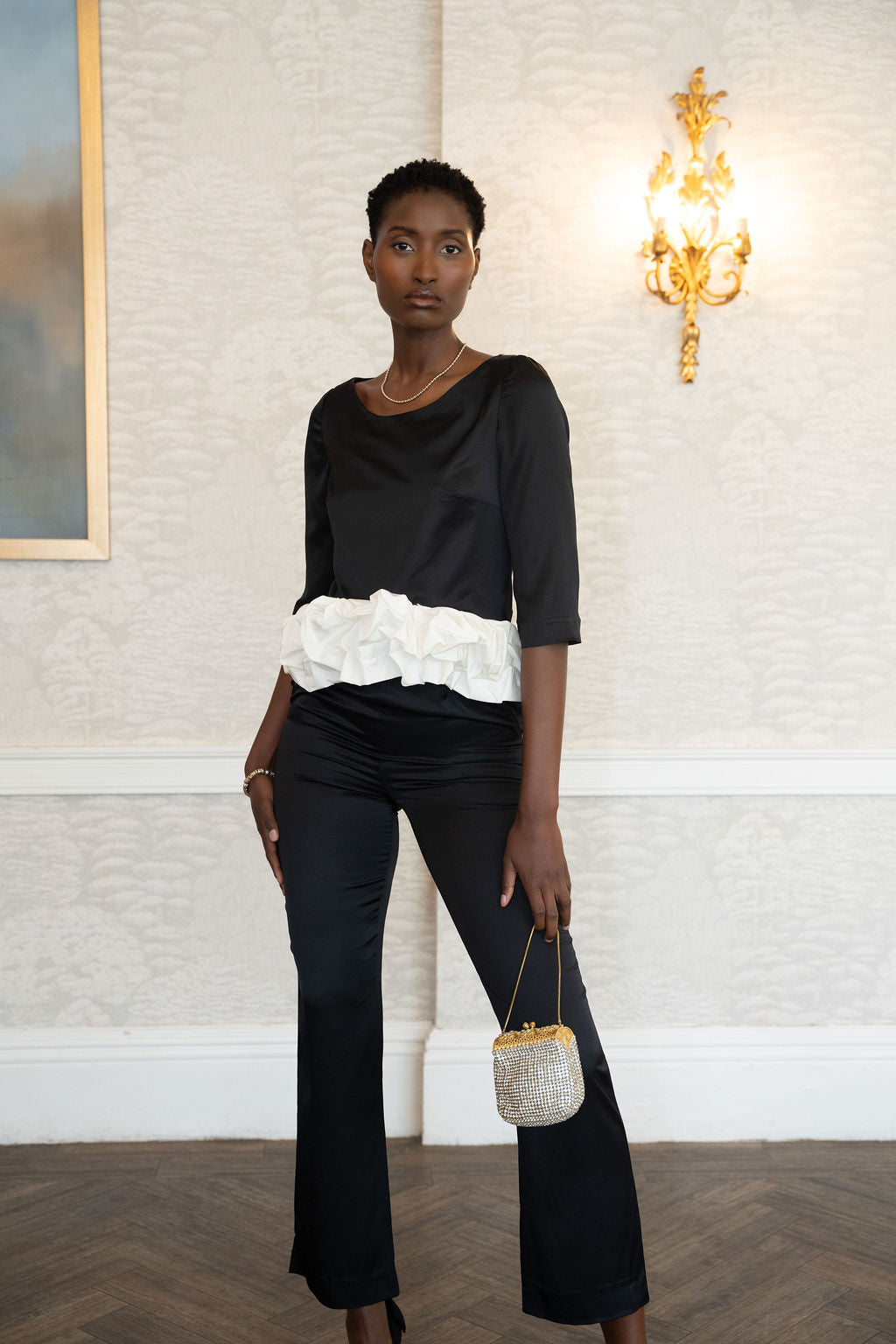 Black satin long-sleeve top with a voluminous white ruffle waist detail.