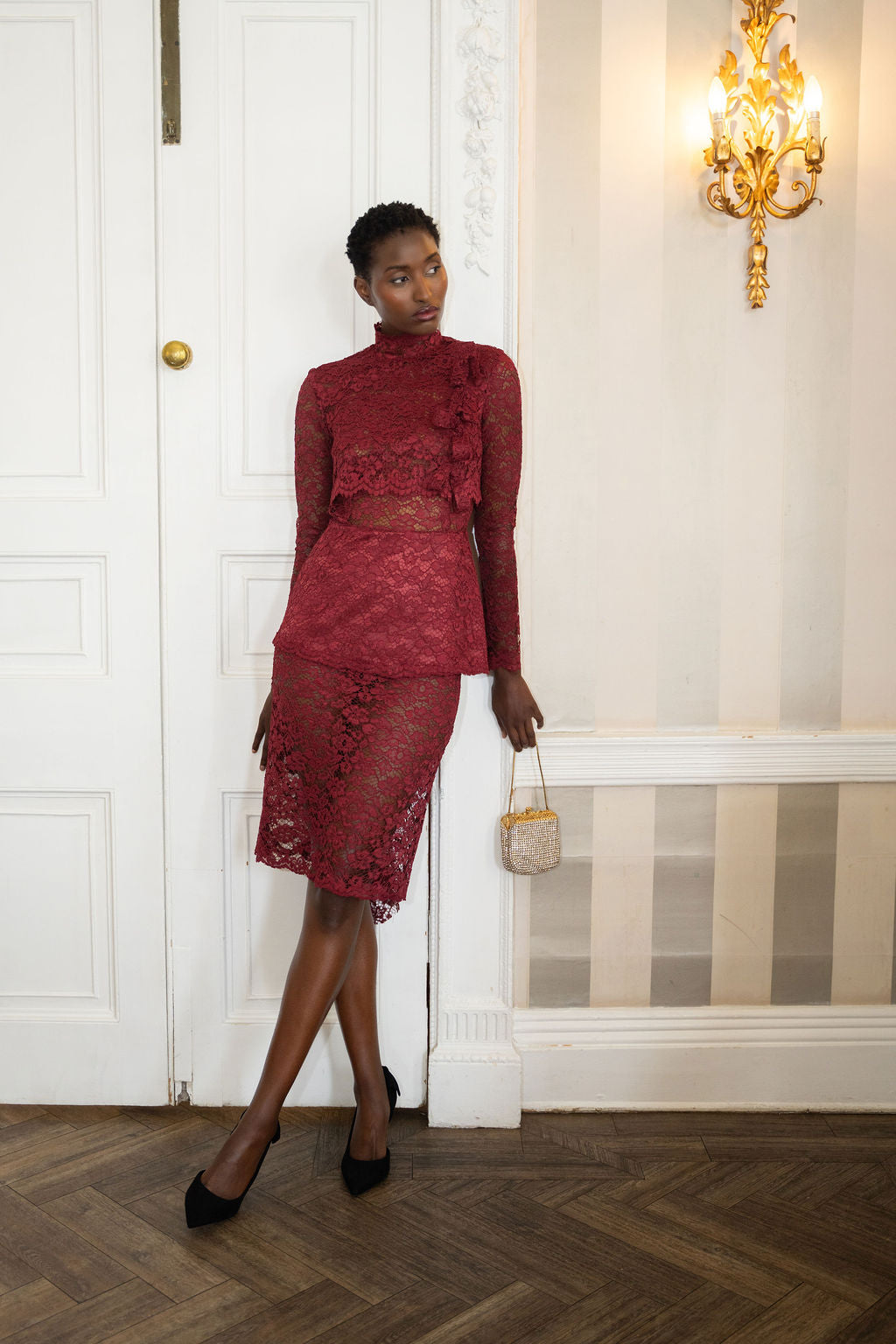 Burgundy midi lace dress with long sleeves and high neckline, paired with black heels and a small beige handbag.