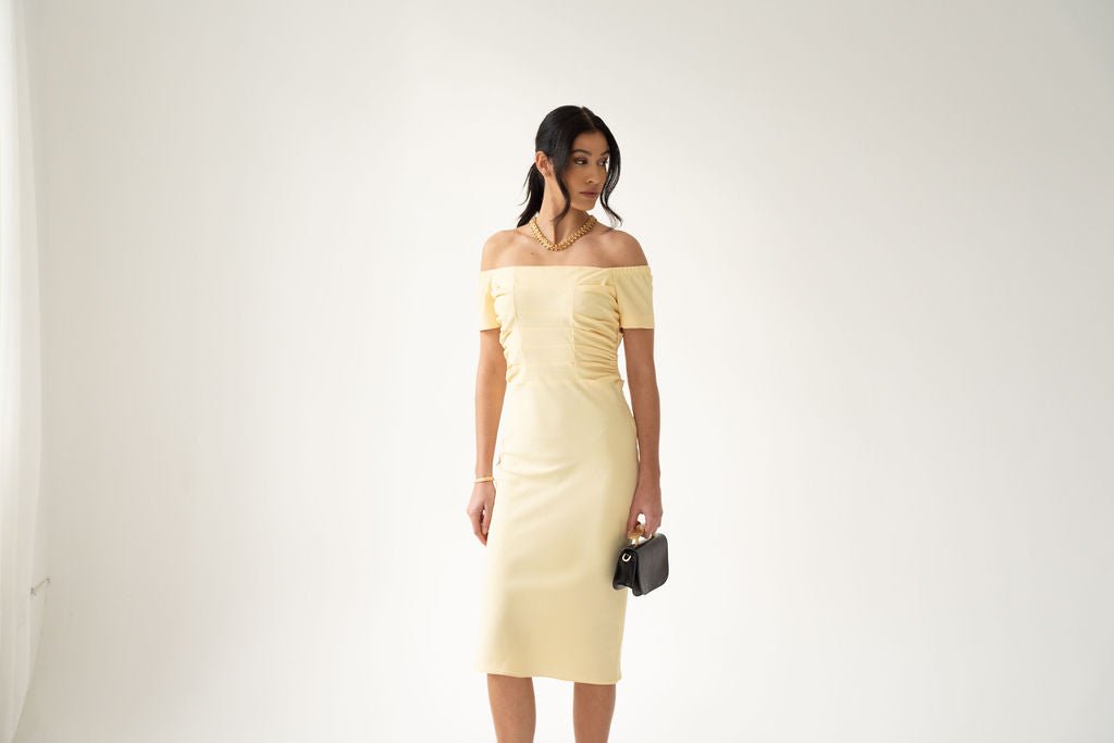 Light yellow off-the-shoulder midi dress with ruched bodice and fitted skirt.