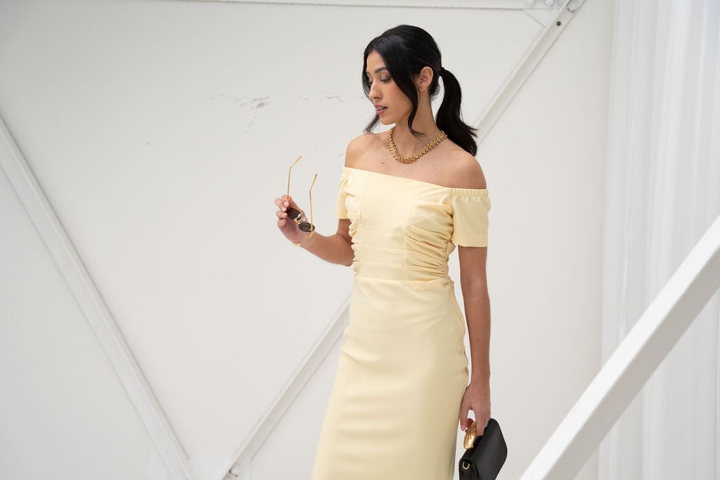 Pale yellow off-the-shoulder midi dress with ruched sides and fitted silhouette.