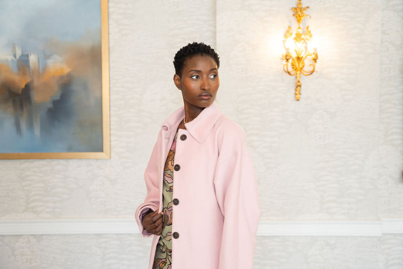 Woman in a pink coat standing in a room with a painting.