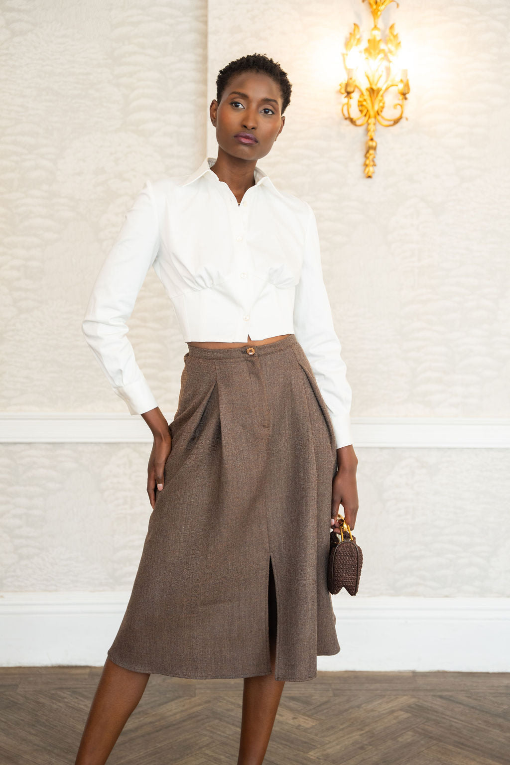 Woman wearing a white blouse and brown skirt in an elegant interior setting.